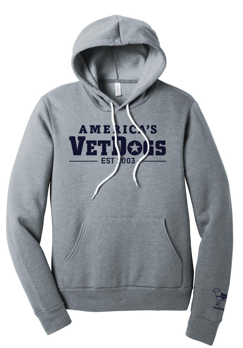 The photo depicts a grey hooded sweatshirt facing forward. Emblazoned on the front is "America's VetDogs, EST. 2003" in navy blue lettering. A front pocket accents the lower part, and white drawstrings adorn the neckline. On the left sleeve's lower portion, a navy cartoon image of a service dog is accompanied by the text "VetDogs.org" in navy as well.